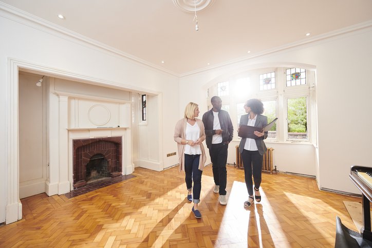 A couple speaking with their realtor while looking around the empty living room of a home.