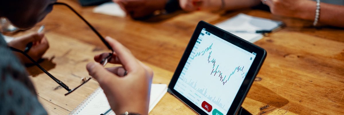 Group of young people sitting around a tablet computer showing financial graph.