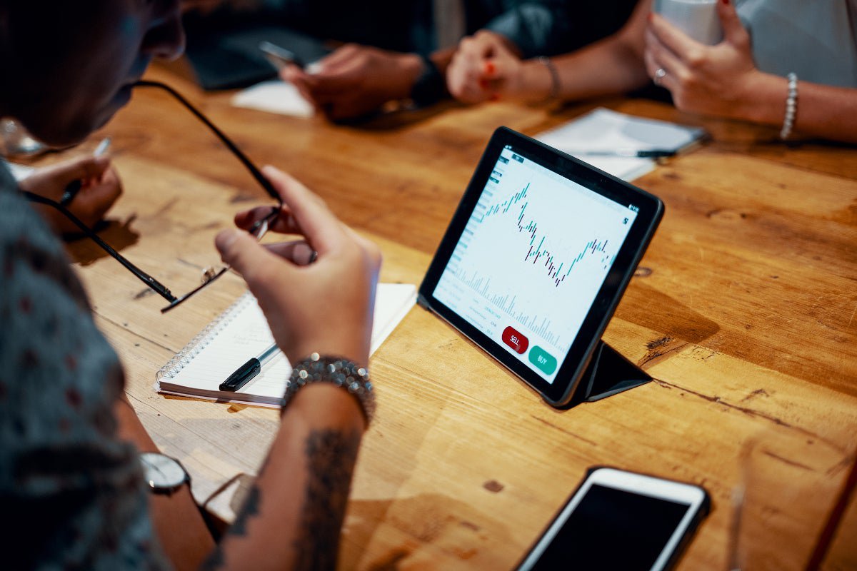 Group of young people sitting around a tablet computer showing financial graph.