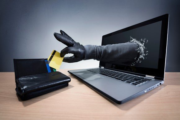 a hand in a black glove reaching out through a laptop screen to take a credit card out of a wallet