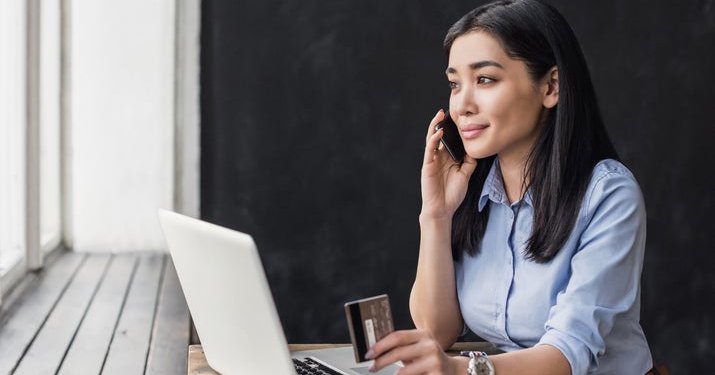A woman holding a credit card and making a phone call.