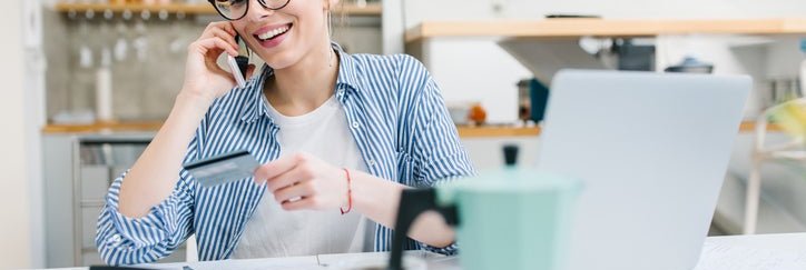 A young woman making a call with her credit card and a laptop.