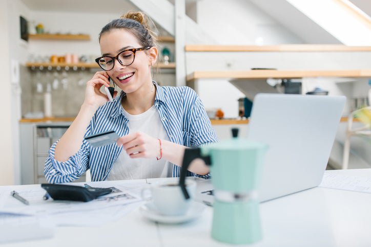 A young woman making a call with her credit card and a laptop.