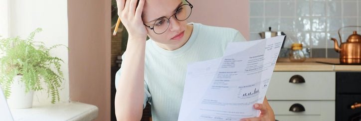 A woman sitting at a table examines lots of bills.
