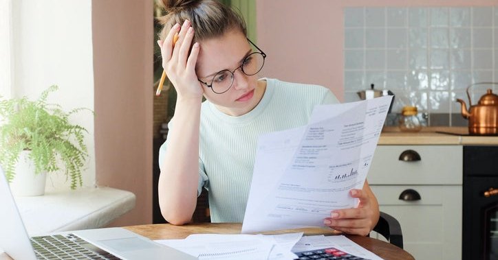 A woman sitting at a table examines lots of bills.