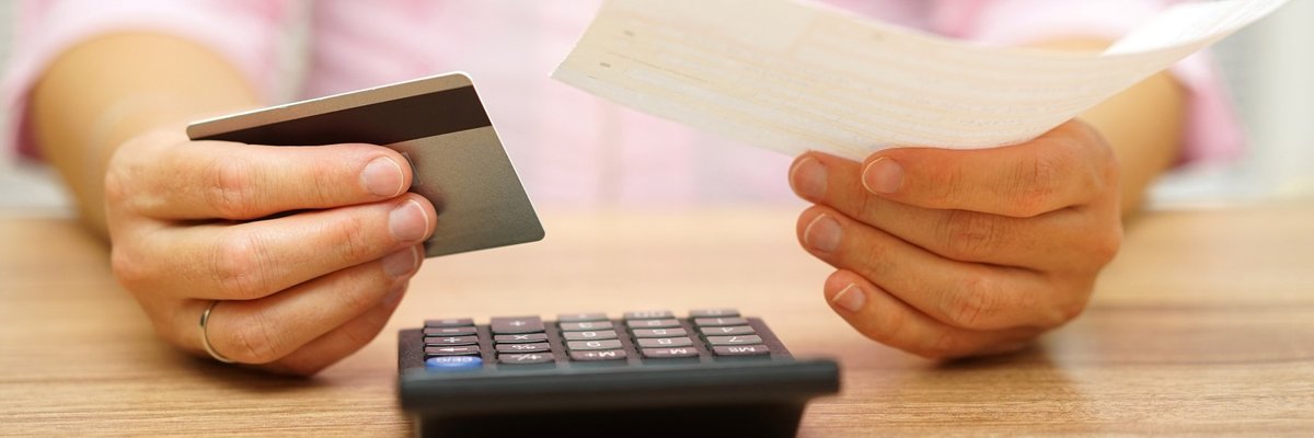 woman holding credit card and piece of paper looking at calculator