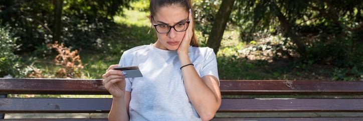 A young woman holding a credit card looks surprised while she checks a laptop.