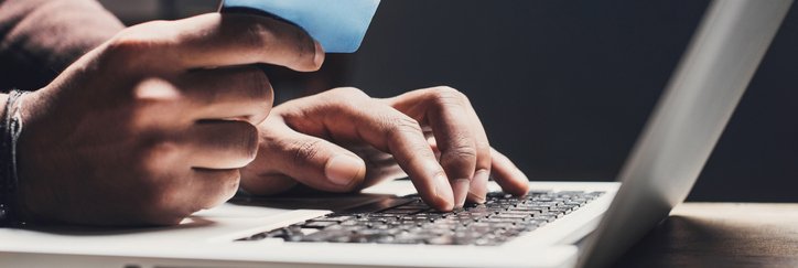 Someone types on a laptop while holding a credit card.