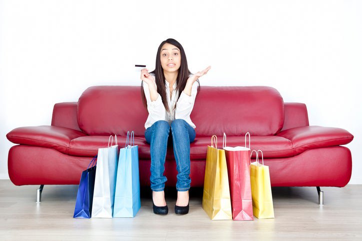 A woman with a credit card on a couch, surrounded by shopping bags.
