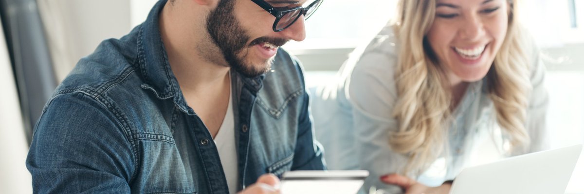Man holding a credit card and woman next to him, both smiling at a laptop