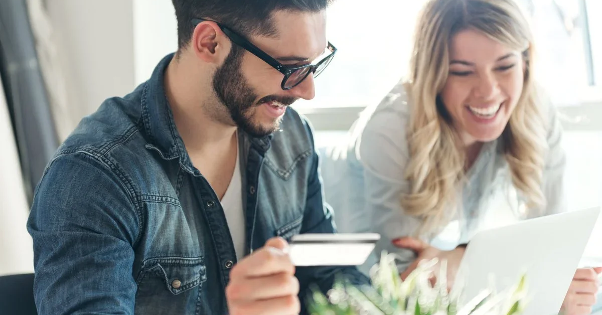 A man holding a credit card and a woman look at a laptop