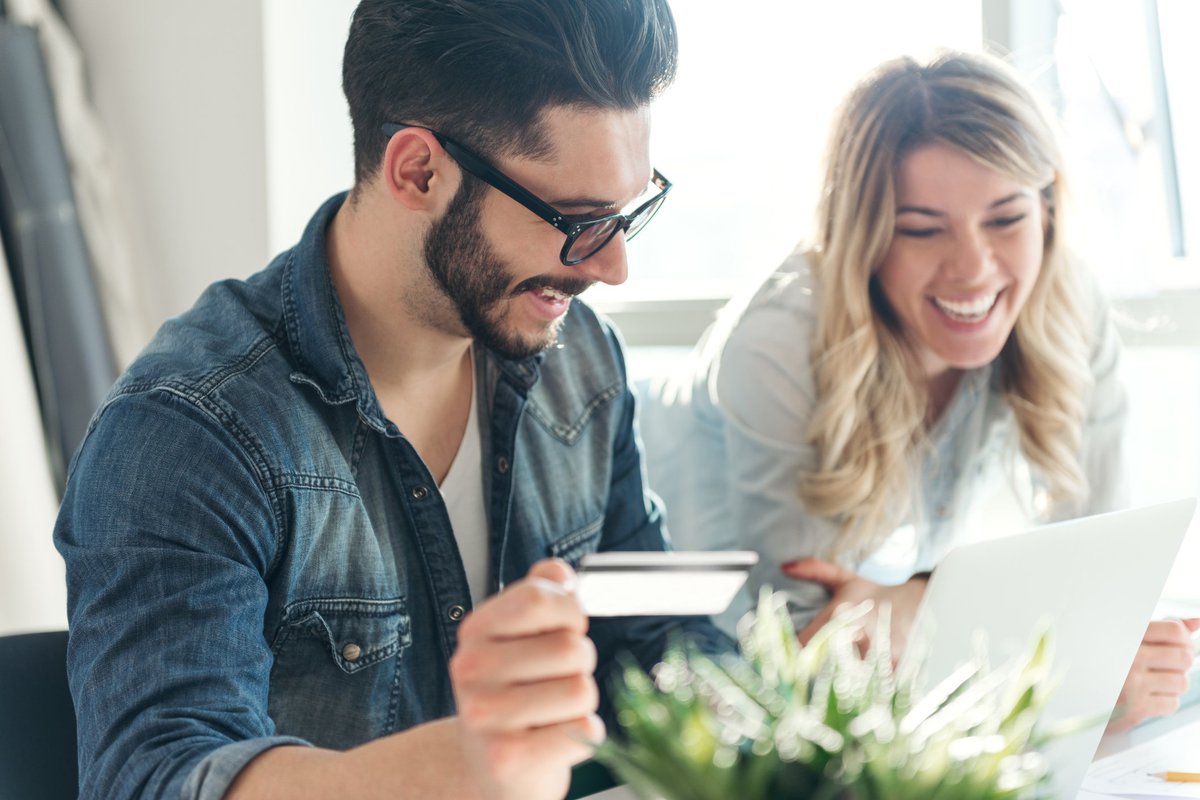 A smiling young couple looking at a laptop while holding a credit card.