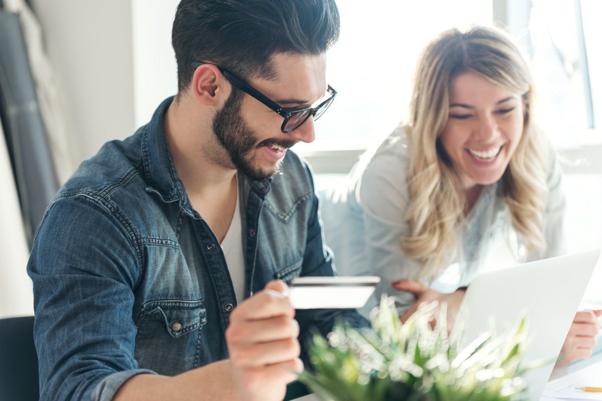 A young man and woman use a credit card while shopping on a laptop.