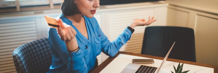 A woman looking frustrated with a credit card in her hand while looking at a laptop.