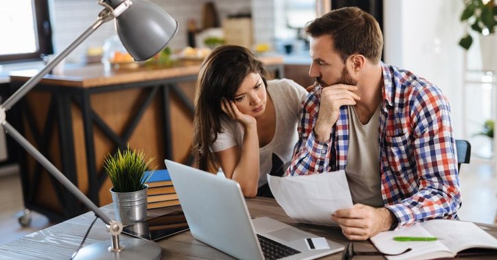 A worried couple looks at bills, with a laptop and a credit card on the table.