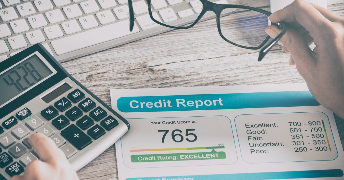 Credit report that reads 765 on a desk where someone is typing on a calculator and their holding glasses