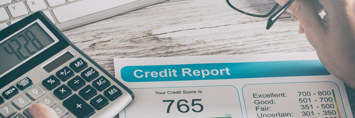 Credit report that reads 765 on a desk where someone is typing on a calculator and their holding glasses