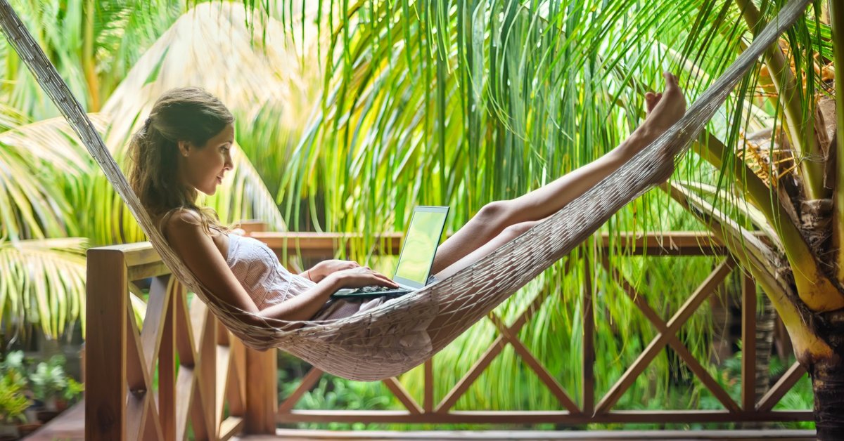 digital nomad using a laptop in a hammock surrounded by palm trees -- vacation remote work
