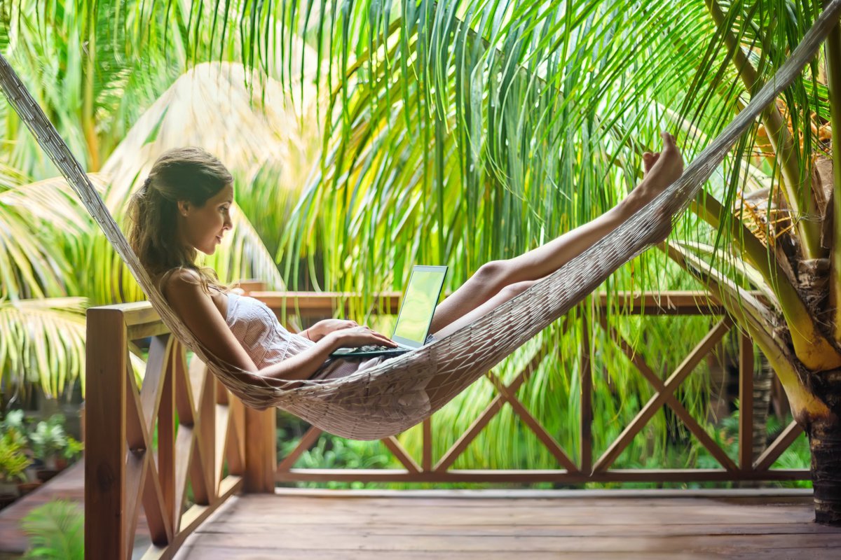 Digital nomad using a laptop in a hammock surrounded by palm trees -- telecommuting on vacation