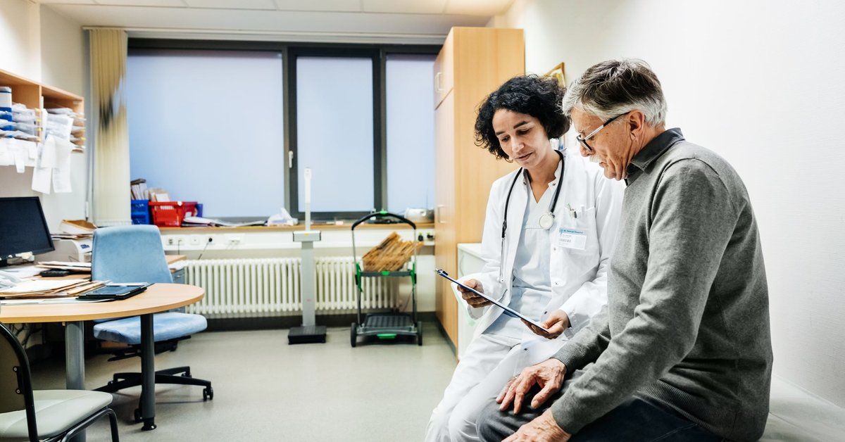 A doctor sitting next to a patient in an exam room and going over test results on a clipboard.