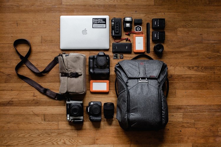 A photographer’s equipment, including multiple cameras, a laptop, and two bags, lay on a hardwood floor.
