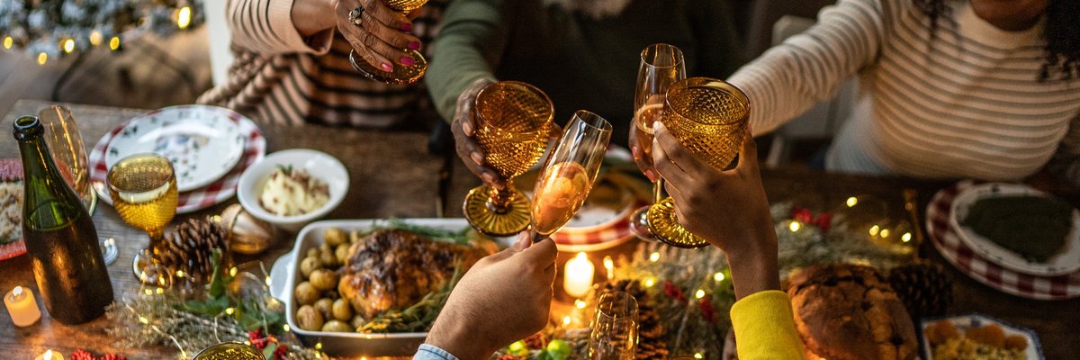 A smiling family toasting their drinks while sitting around a holiday dinner table filled with food.