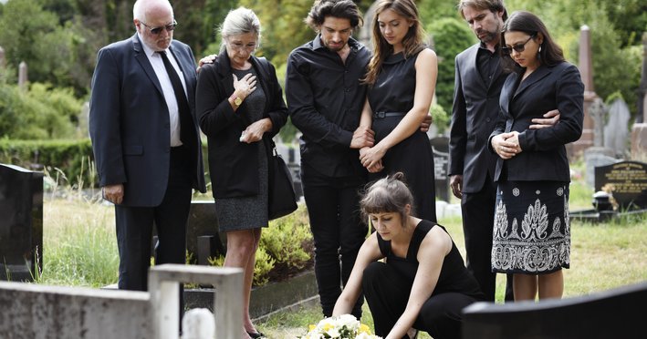A family standing around a gravestone while one woman lays down flowers.