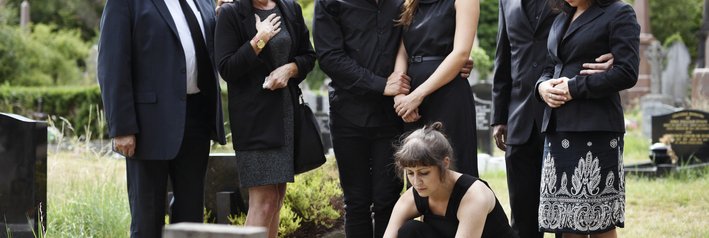 A family standing around a gravestone while one woman lays down flowers.