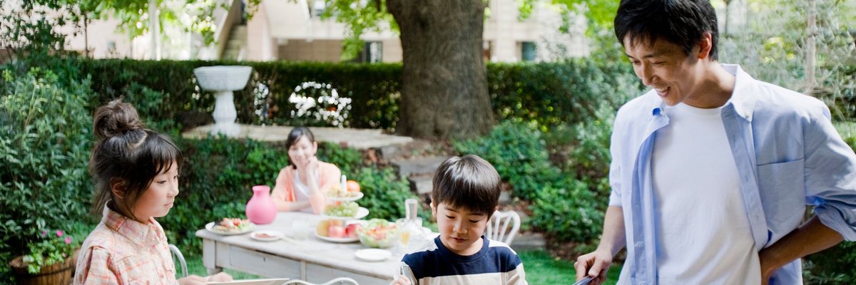 Two parents and two kids enjoying a backyard barbecue surrounded by green trees.