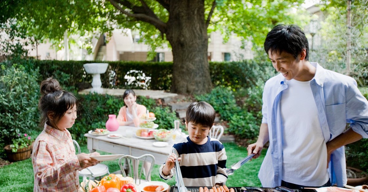 Two parents and two kids enjoying a backyard barbecue surrounded by green trees.