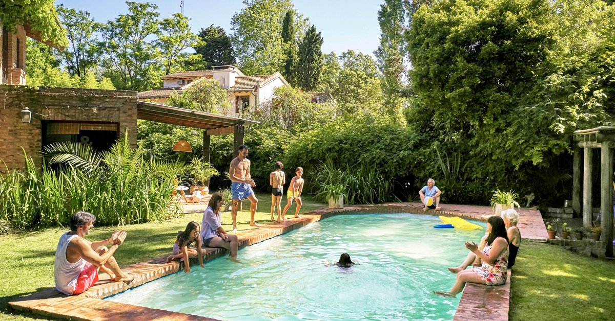 A family playing in a backyard pool surrounded by green bushes and trees.