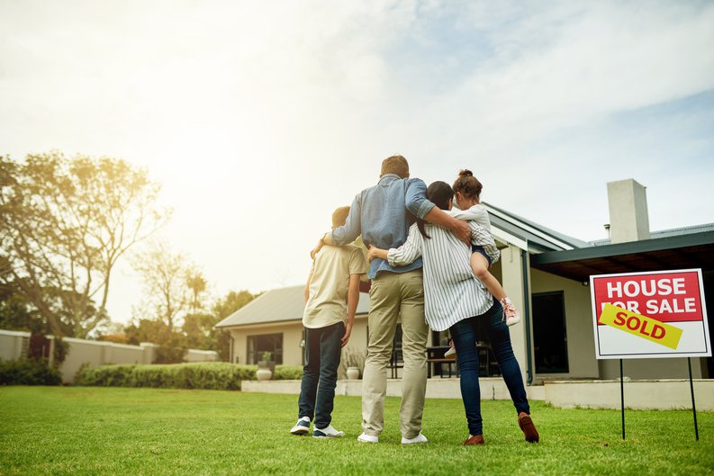 A family of four standing in front of their new home.