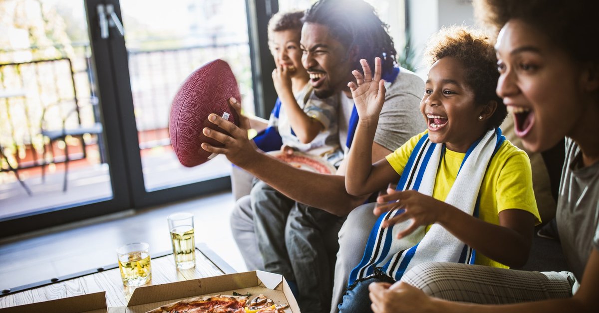 A family of four sitting on the couch and cheering on a football game.