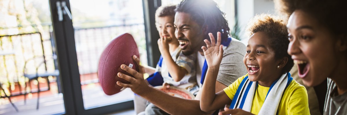 A family of four sitting on the couch and cheering on a football game.