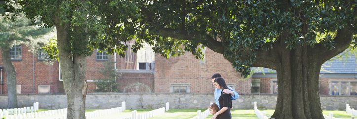 A family of three visiting a gravestone in a cemetery.