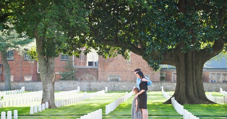 A family of three visiting a gravestone in a cemetery.