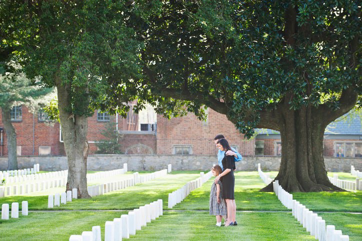 A family of three visiting a gravestone in a cemetery.