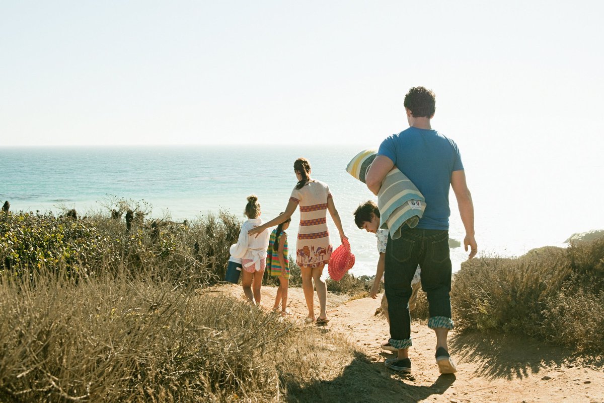 Two parents and three children carrying towels and walking to the beach.