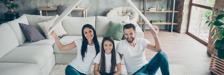 A couple with a young daughter holds up a cardboard roof.