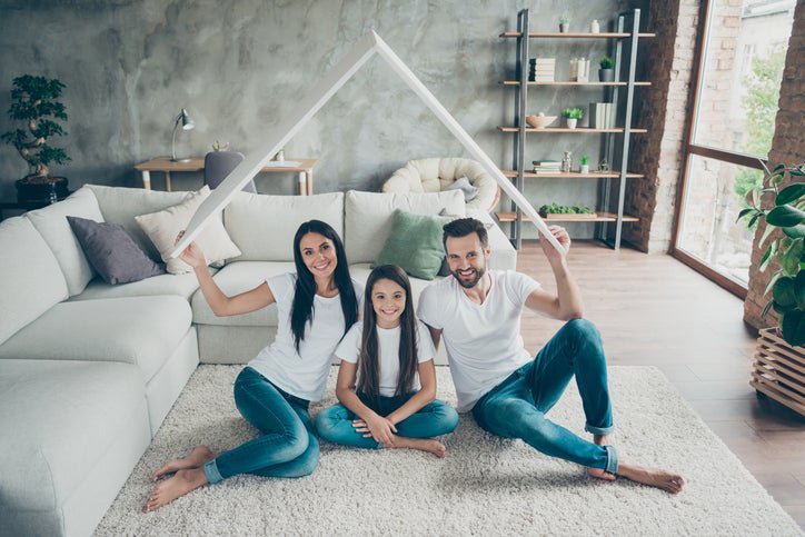 A couple with a young daughter holds up a cardboard roof.