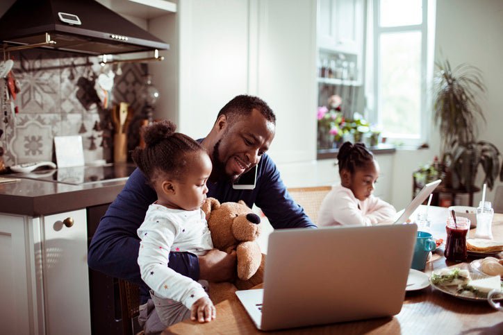 A father working on his laptop while managing two young children.