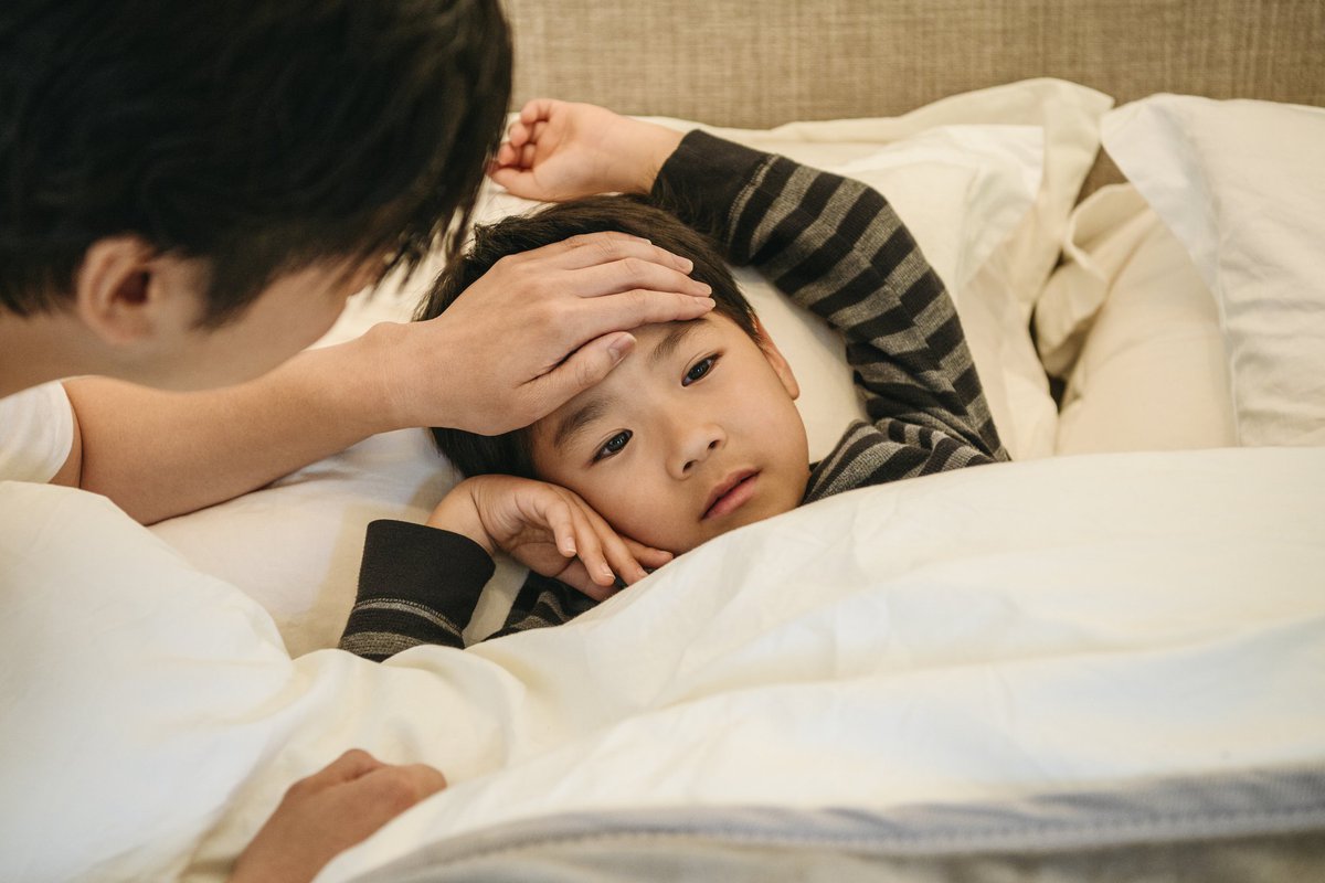 A child in bed with his dad's hand on his forehead to check his temperature.