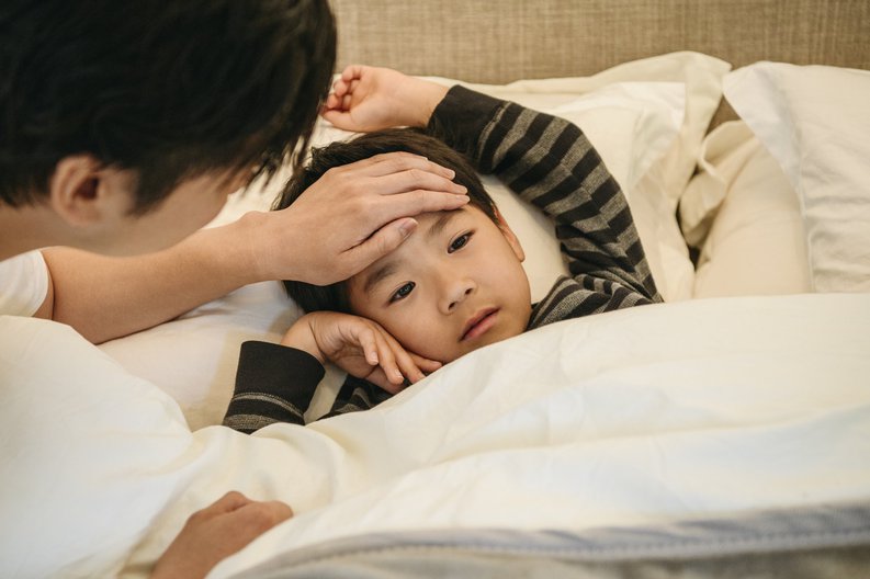 A child in bed with his dad's hand on his forehead to check his temperature.