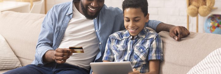 A father and son looking at a laptop and a credit card.