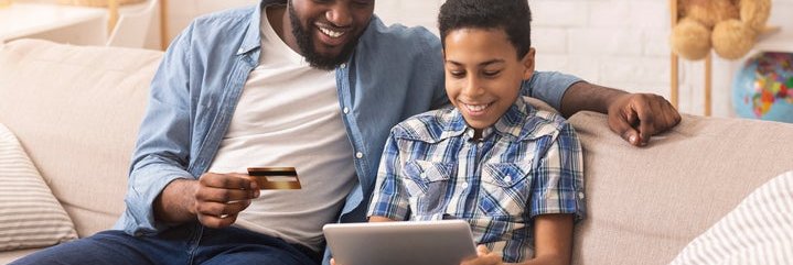A father and son looking at a laptop and a credit card.