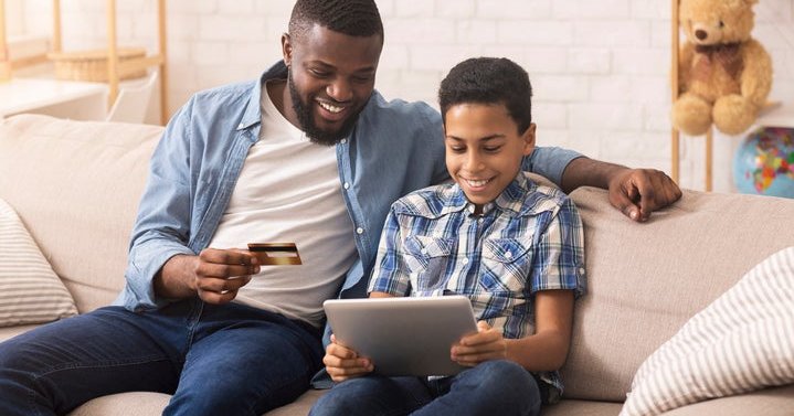 A father and son looking at a laptop and a credit card.