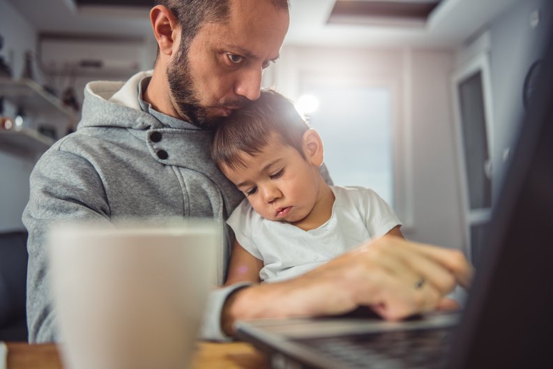 father working from home on laptop and kissing toddler sitting in his lap -- telecommuting