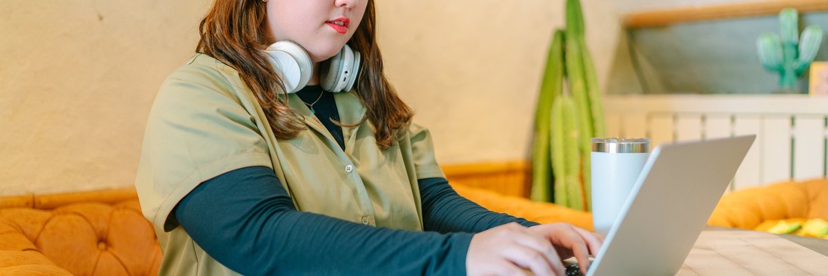 A female college student sitting at a table at home and studying on her laptop.