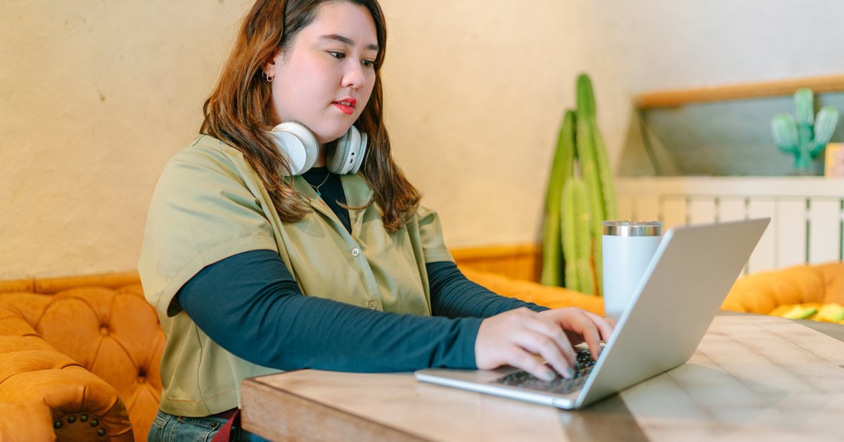 A female college student sitting at a table at home and studying on her laptop.