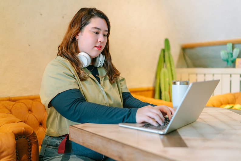 A female college student sitting at a table at home and studying on her laptop.
